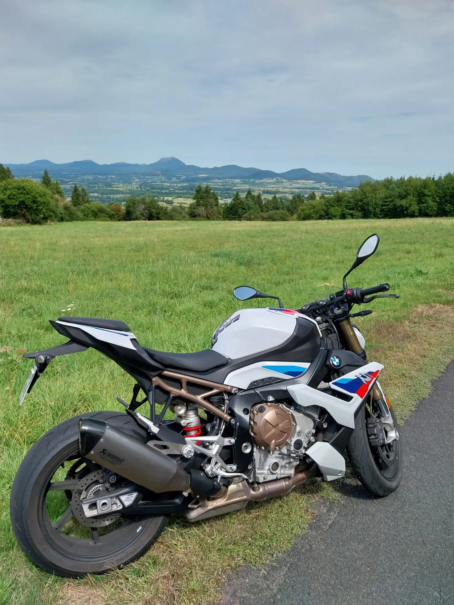 Moto blanche garée dans un paysage vert avec collines.